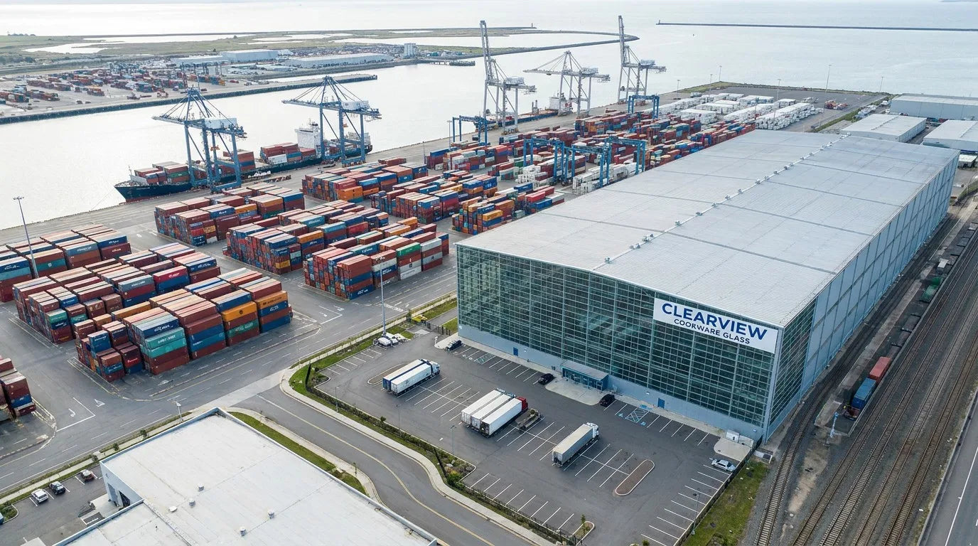 Aerial view of shipping containers and factory warehouse illustrating the FOB cost stack for tempered glass cookware lids from a China factory